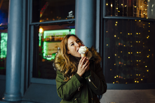 Young blonde woman eating ice cream at night with Christmas ligh